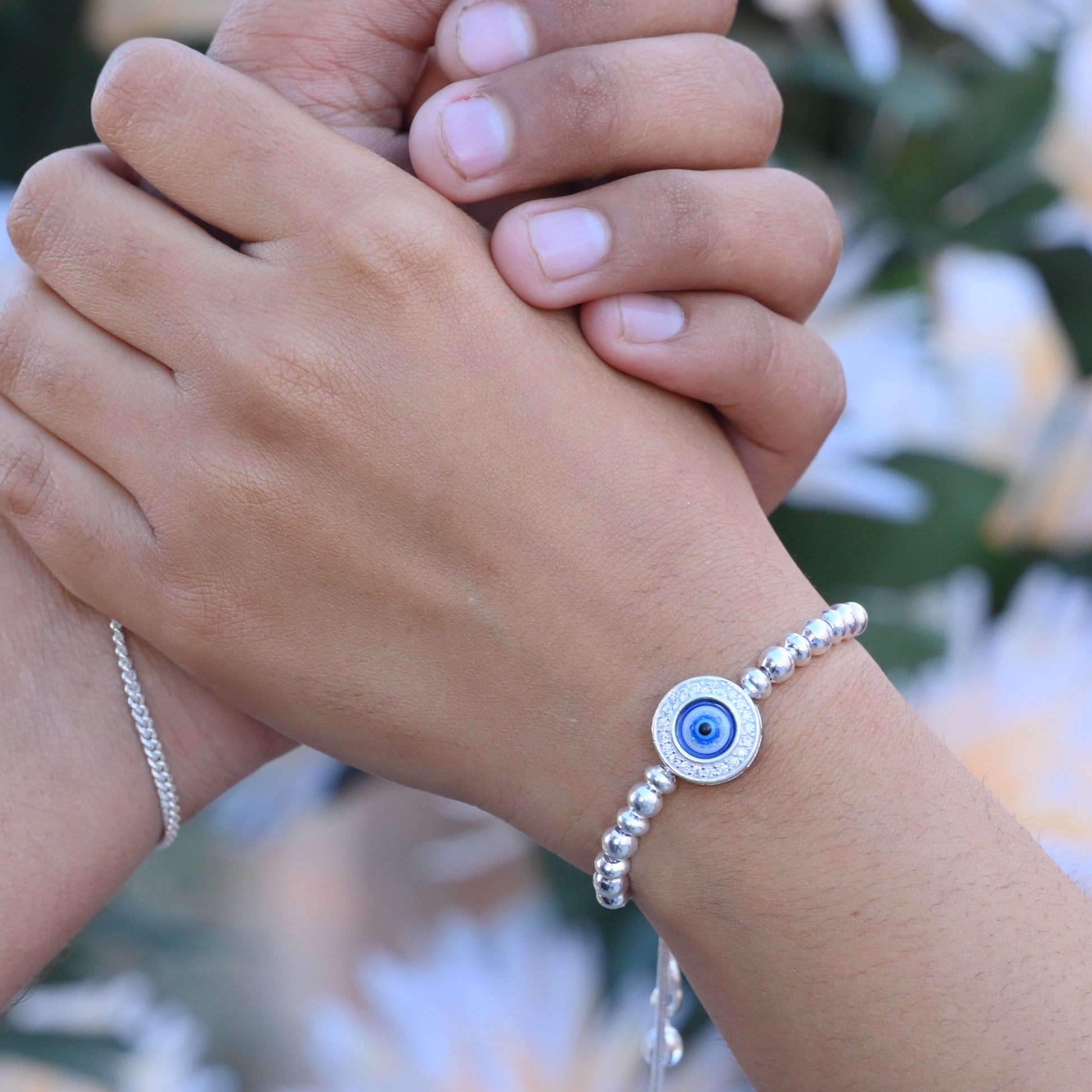 Elegant silver bracelet featuring floral design and evil eye stone for protection.
